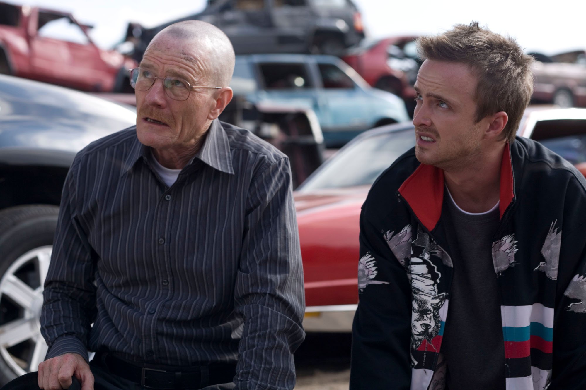 Bryan Cranston and Aaron Paul as Walter White and Jesse Pinkman in 'Breaking Bad' Season 2. They're sitting on the back of a car and both look disappointed.