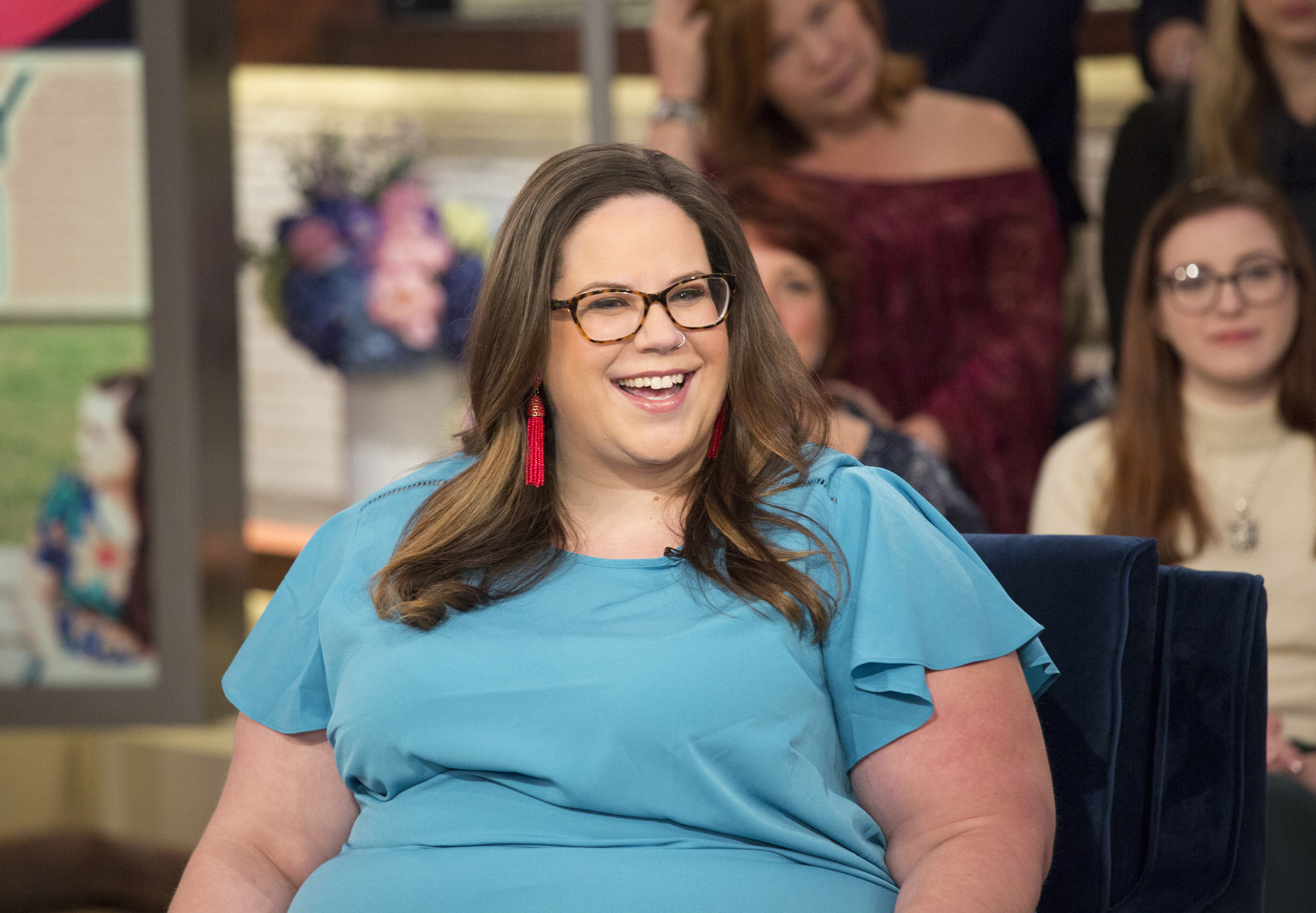 'My Big Fat Fabulous Life' star Whitney Thore wearing a blue blouse, red earrings, and glasses during a talk show appearance.
