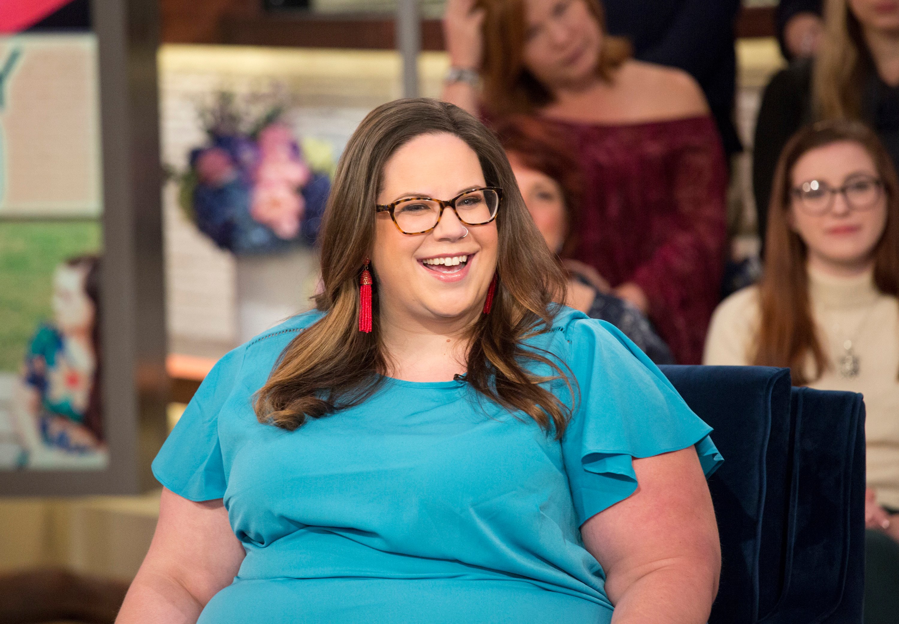 'My Big Fat Fabulous Life' star Whitney Thore wearing a blue blouse, red earrings, and glasses during a talk show appearance.