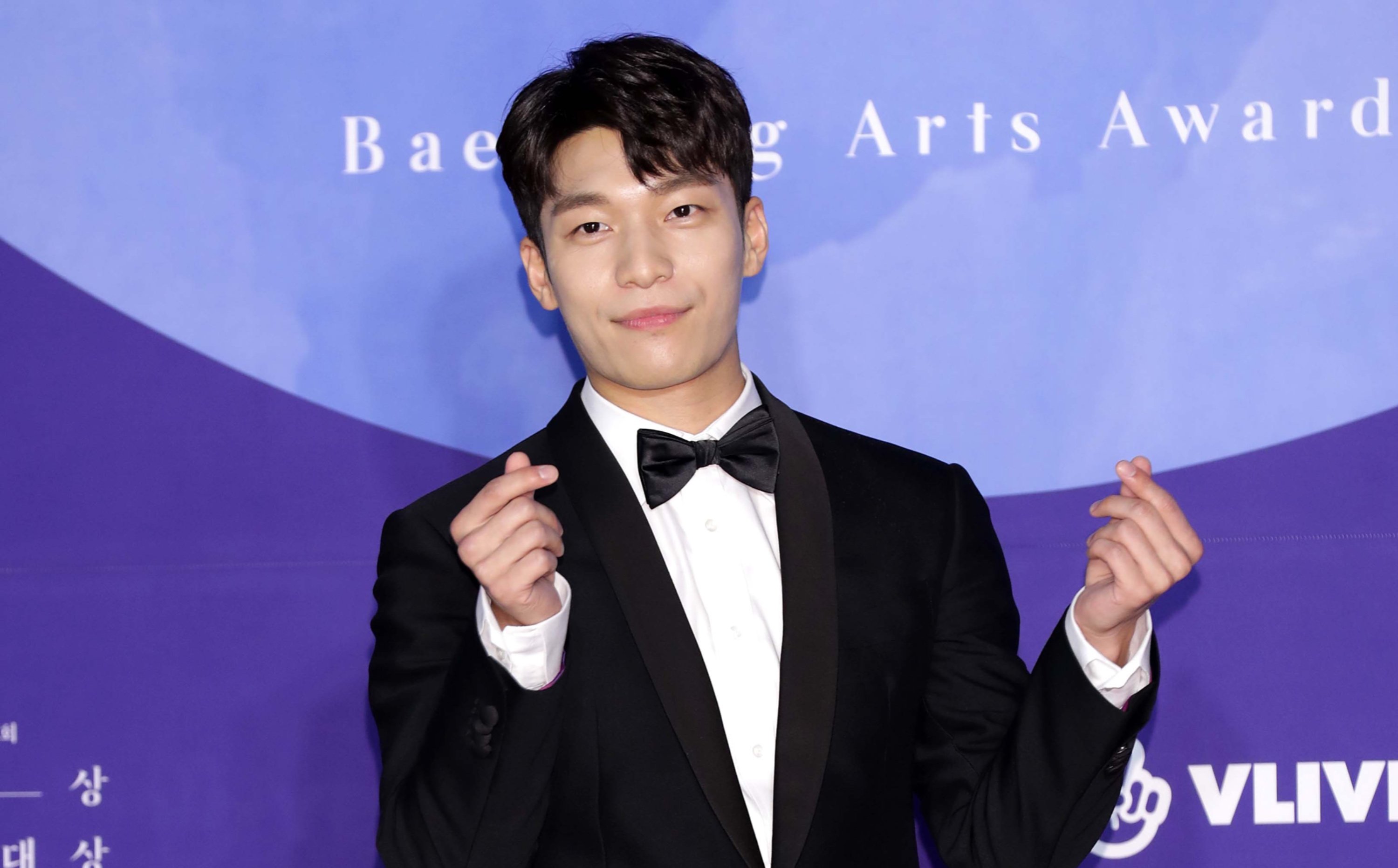 Wi Ha-Joon from Netflix's 'Squid Game' K-drama wearing black tuxedo doing heart fingers.