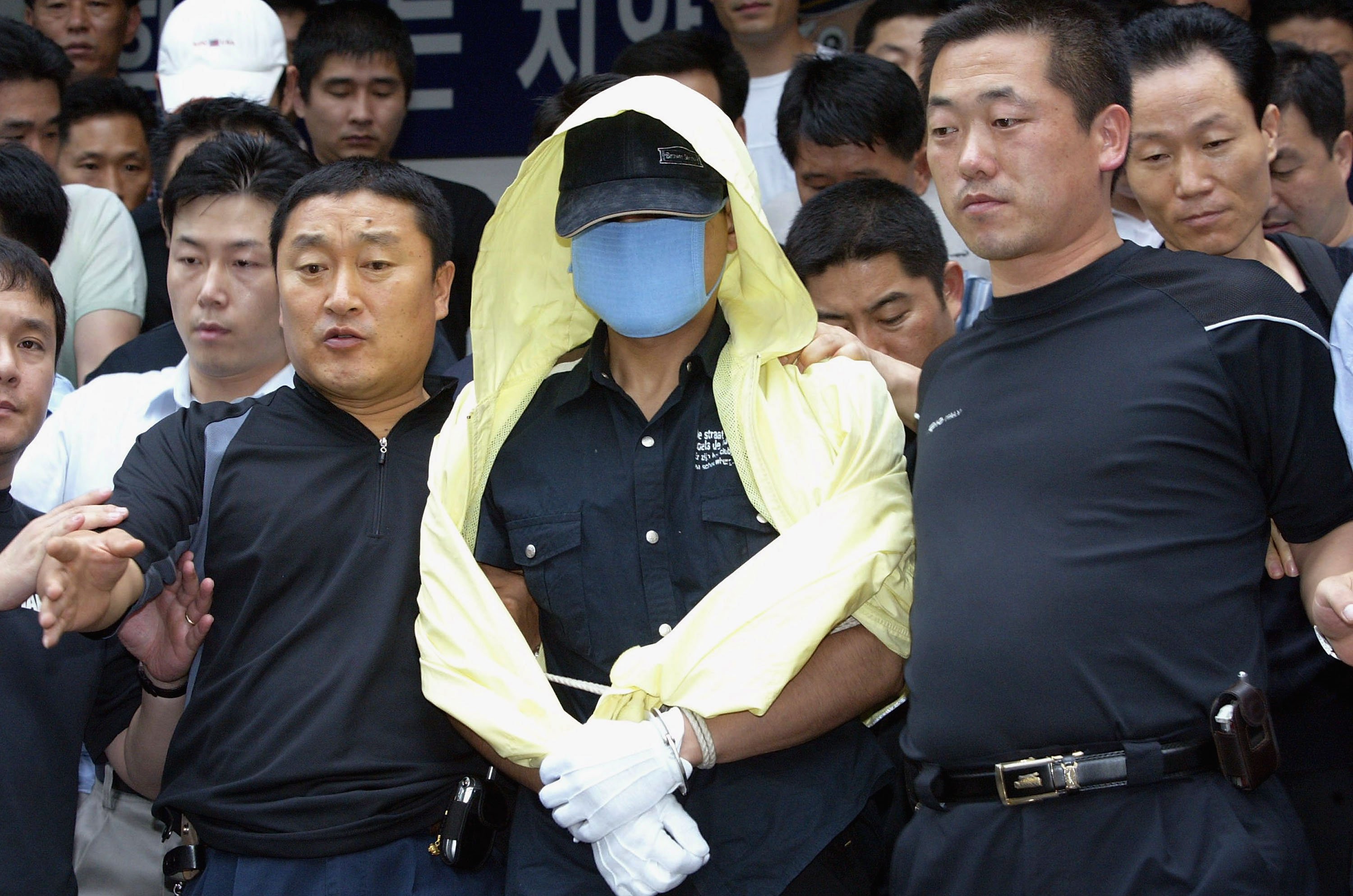 Killer Yoo Young-chul from 'The Raincoat Killer: Chasing a Predator in Korea' surrounded by police wearing yellow raincoat