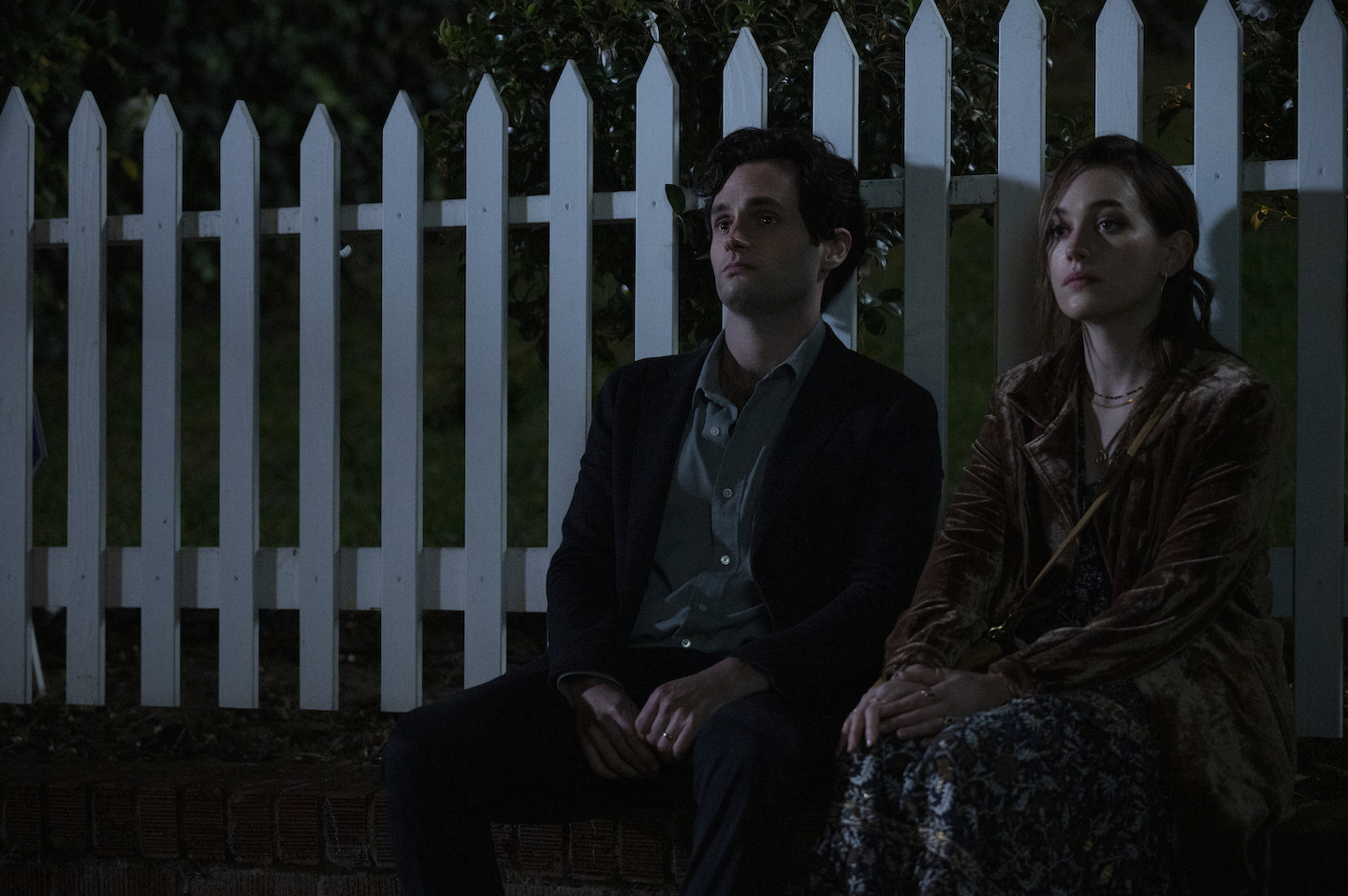 Penn Badgley and Victoria Pedretti, 'You' Season 3 cast members, sitting next to each other outside in the dark
