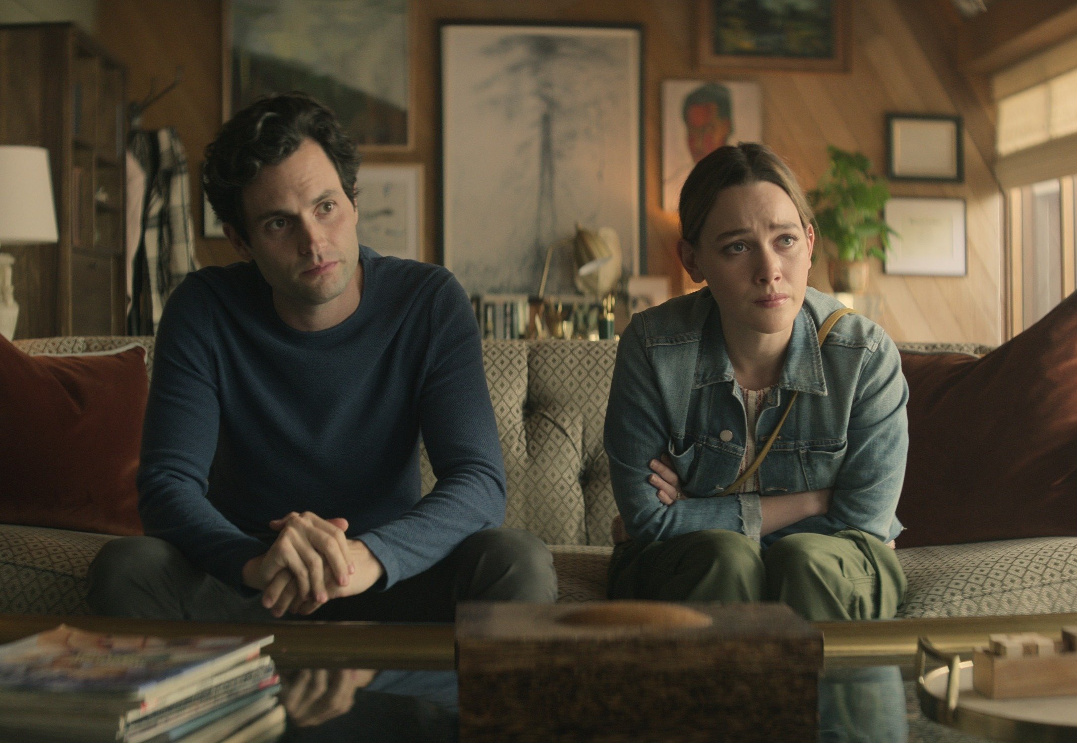 Penn Badgley and Victoria Pedretti in 'You' Season 3 on Netflix. They're sitting on a couch staring forward, where their therapist sits off-screen.