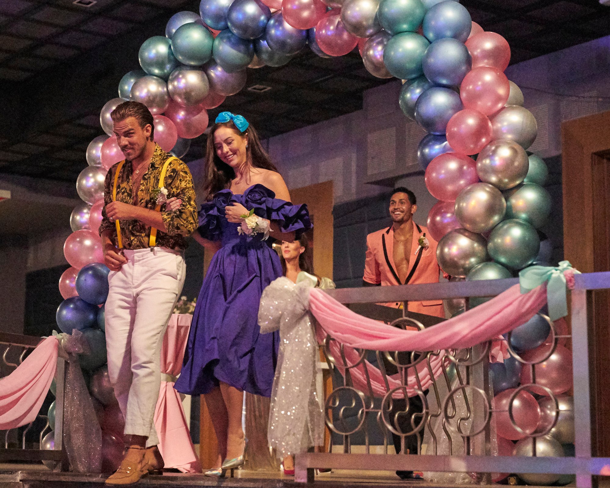 'Bachelor in Paradise' participants Noah Erb and Abigail Heringer walk through a balloon arch at the '80s themed prom in a production still