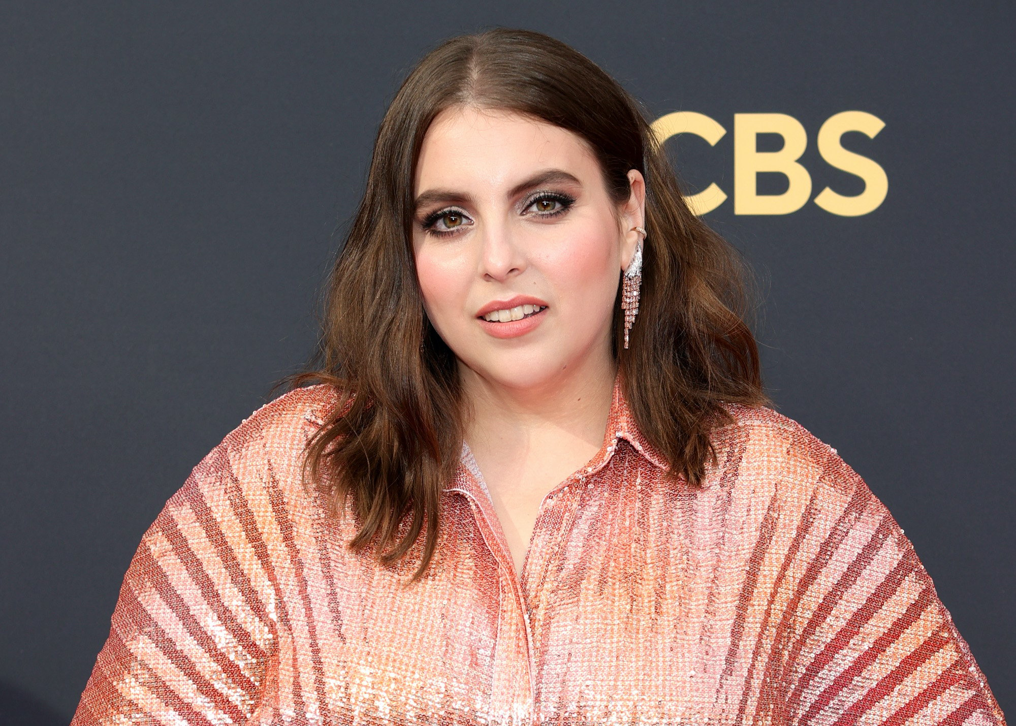 Actor Beanie Feldstein poses in a shimmering pink dress on the 2021 Emmy Awards red carpet.