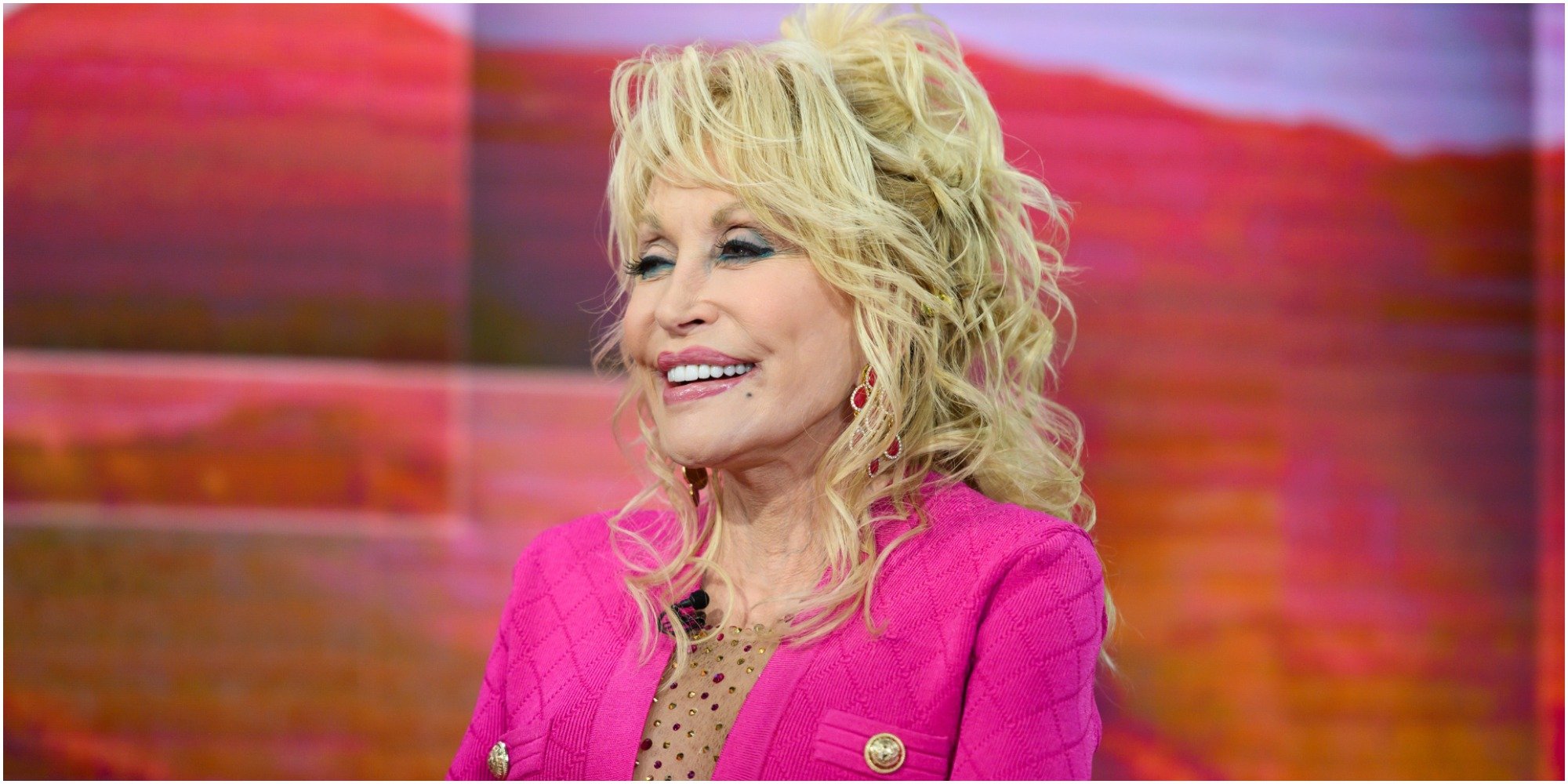 Dolly Parton wears a pink suit and smiles for the camera.