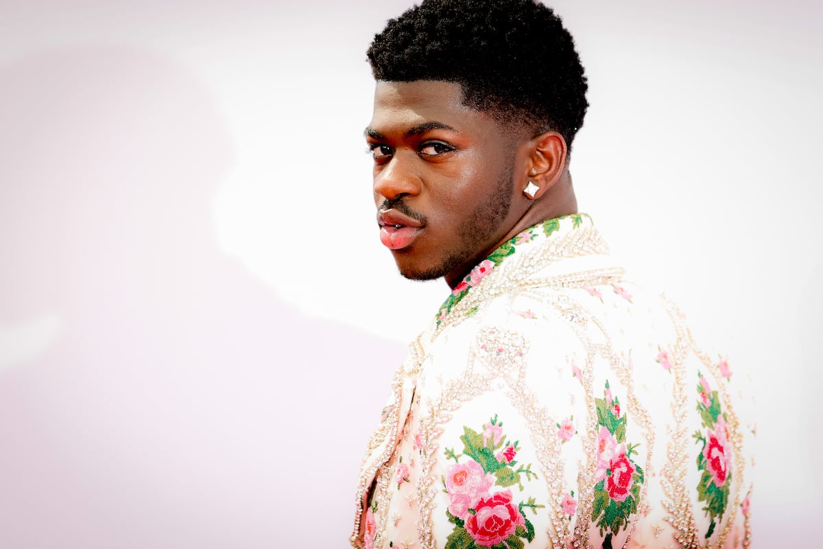 Lil Nas X looking over his shoulder and wearing a jacket with flower designs.