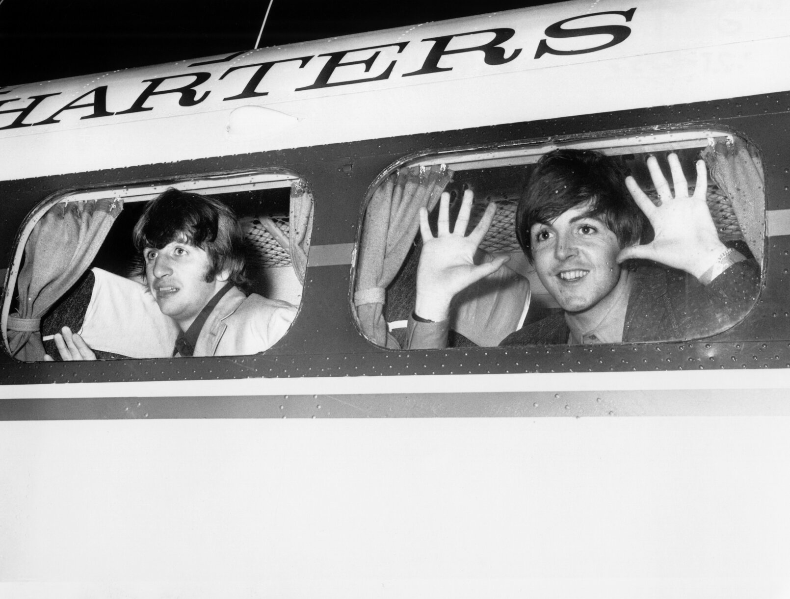 Ringo Starr and Paul McCartney of The Beatles look out the window of a plane.