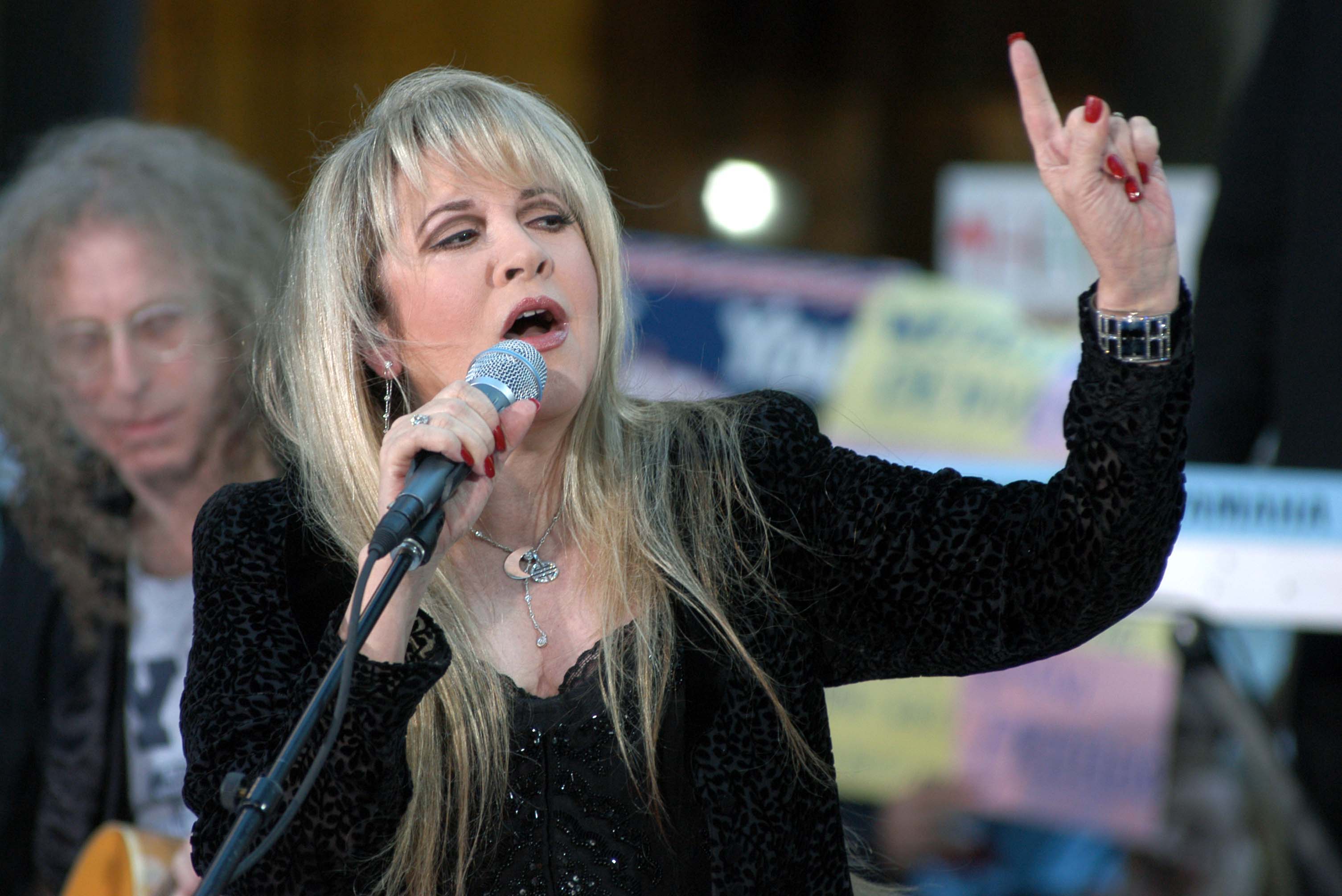 Stevie Nicks performs in a black outfit and Waddy Wachtel sits in the background