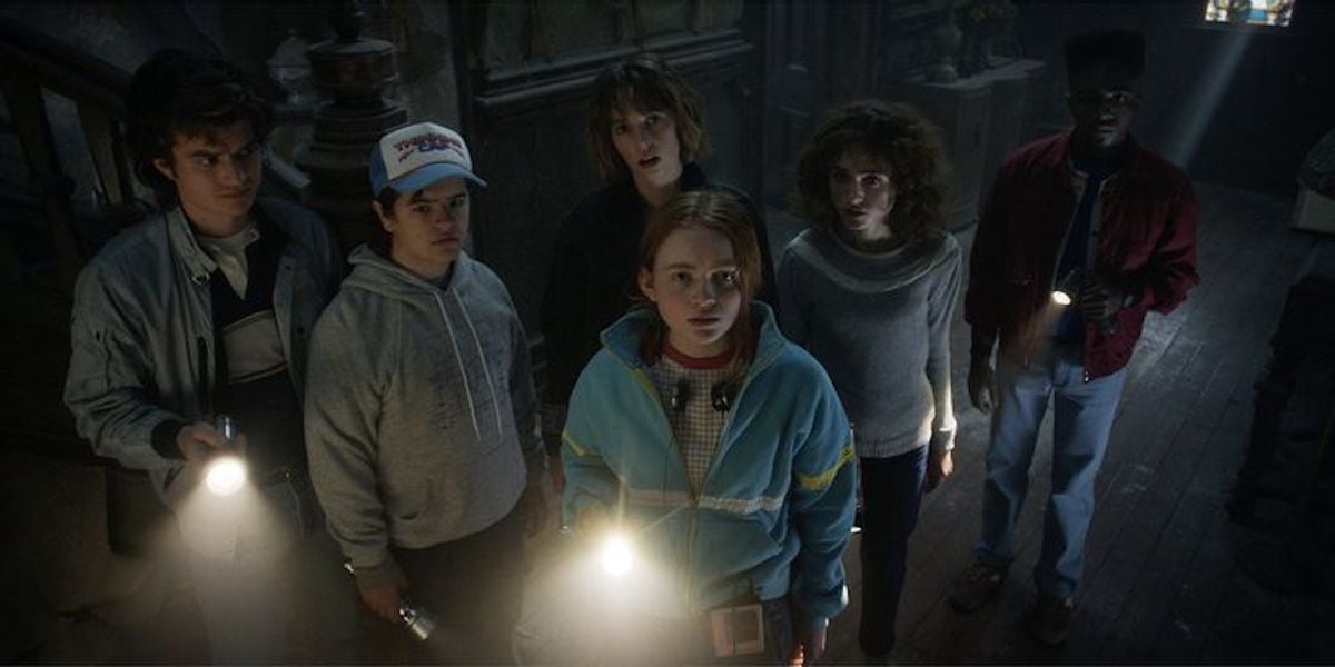 Joe Keery, Gaten Matarazzo, Sadie Sink, Maya Hawke, Natalia Dyer, and Lucas McLaughlin hold flashlights in a production still from 'Stranger Things' Season 4