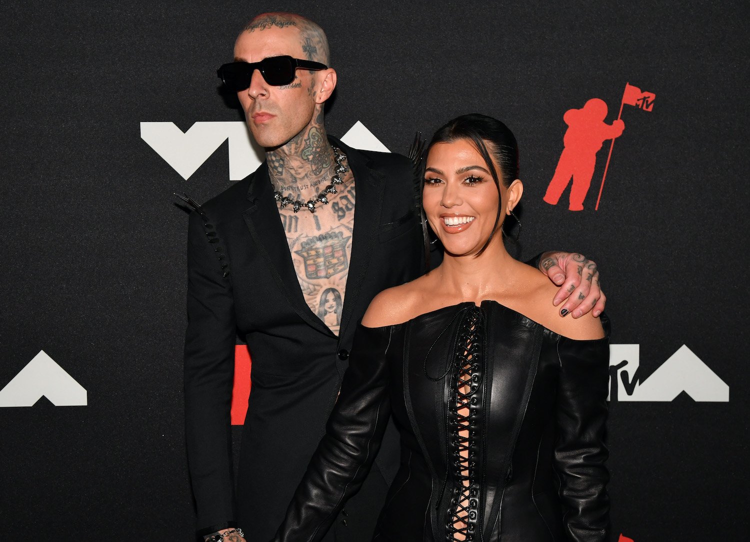 Travis Barker wears a black suit without a shirt and Kourtney Kardashian wears a black lace up dress on the red carpet at the 2021 MTV Video Music Awards