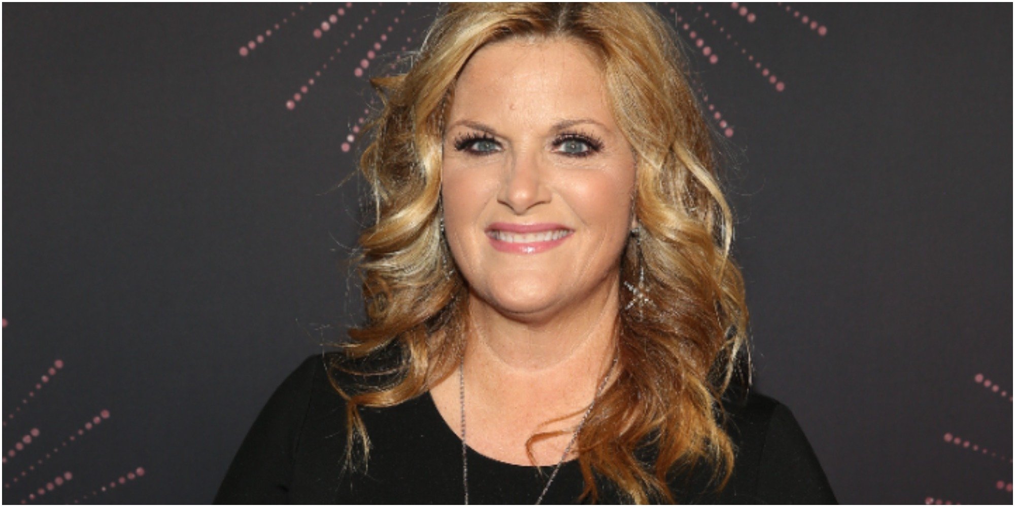 Trisha Yearwood wearing a black top smiling in front of a black background.
