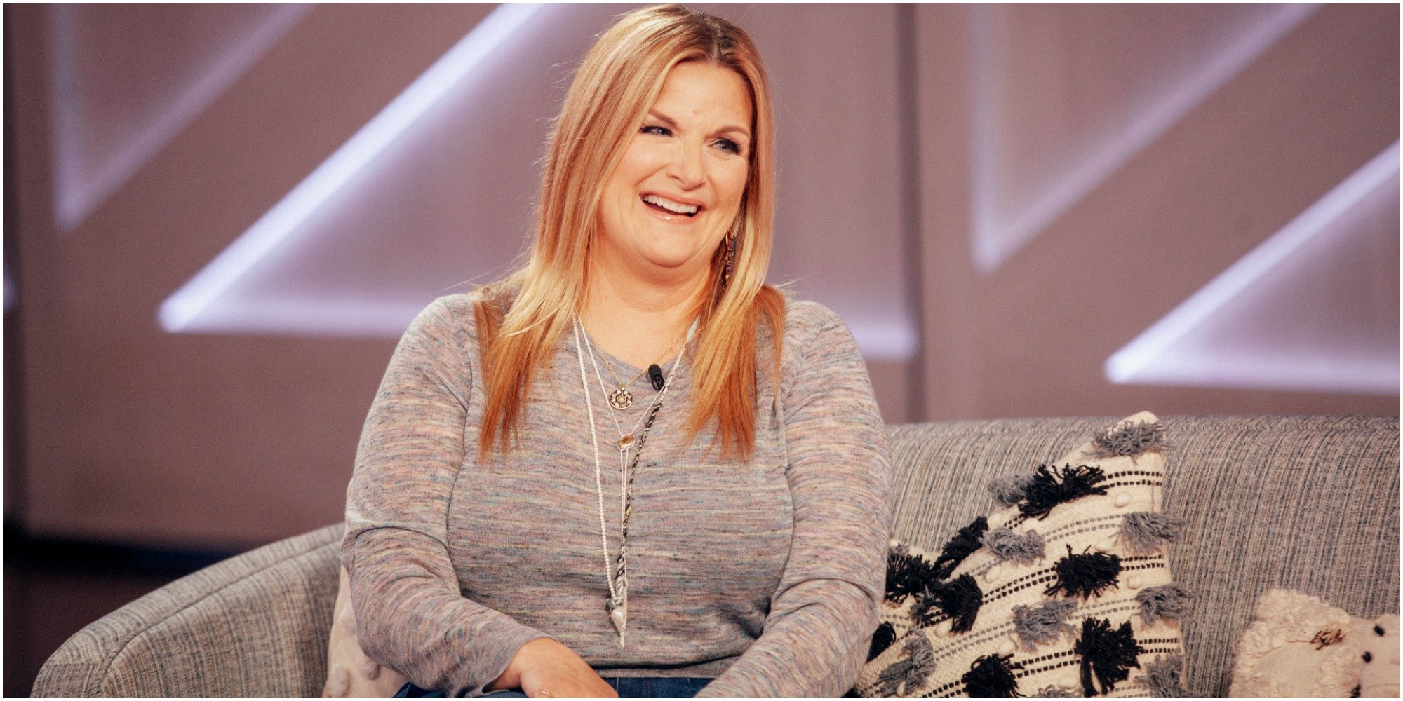 Trisha Yearwood laughs while sitting on a couch during a television appearance.