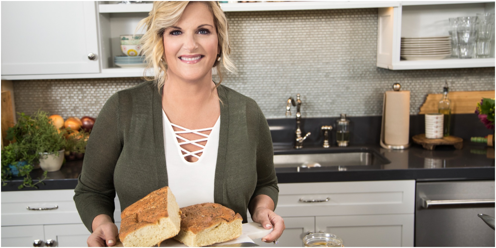 Trisha Yearwood smiles wearing a white shirt and green cardigan holding a plate of food