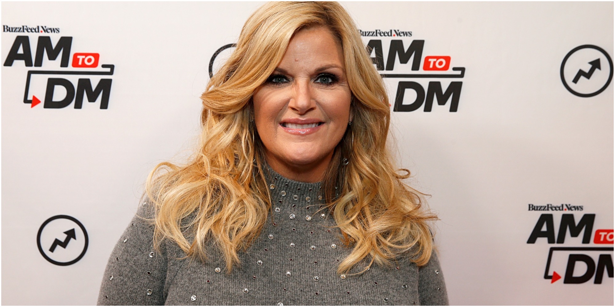 Trisha Yearwood stands in a gray sweater and poses for a photographer.
