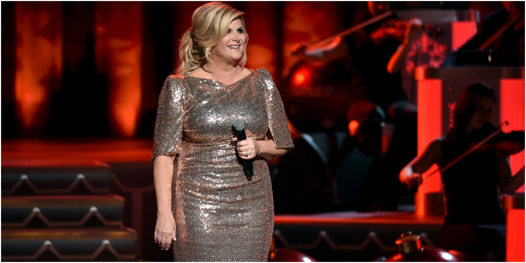 Trisha Yearwood stands on stage wearing a gold dressing and holding a microphone.