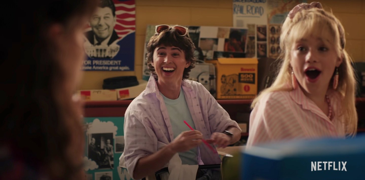 Logan Allen, in a pink button down with sunglasses on his head, and Elodie Orkin, in a pink shirt, as Jake and Angela in a scene from 'Stranger Things' Season 4.