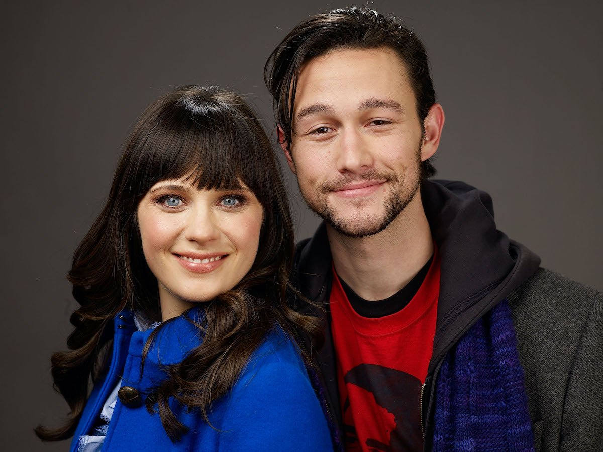 Zooey Deschanel and Joseph Gordon-Levitt smiling in front of a gray background