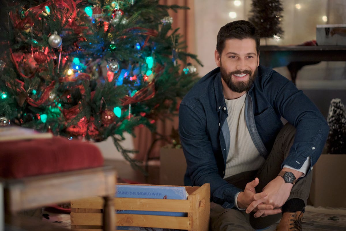 Casey Deidrick kneeling in front of Christmas tree in the Hallmark Channel Christmas movie 'A Very Merry Bridesmaid'