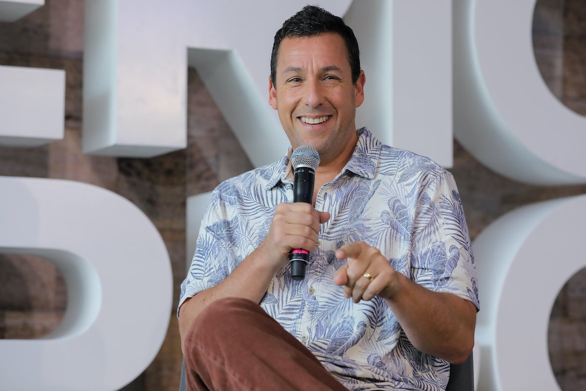 Adam Sandler smiling, holding a microphone