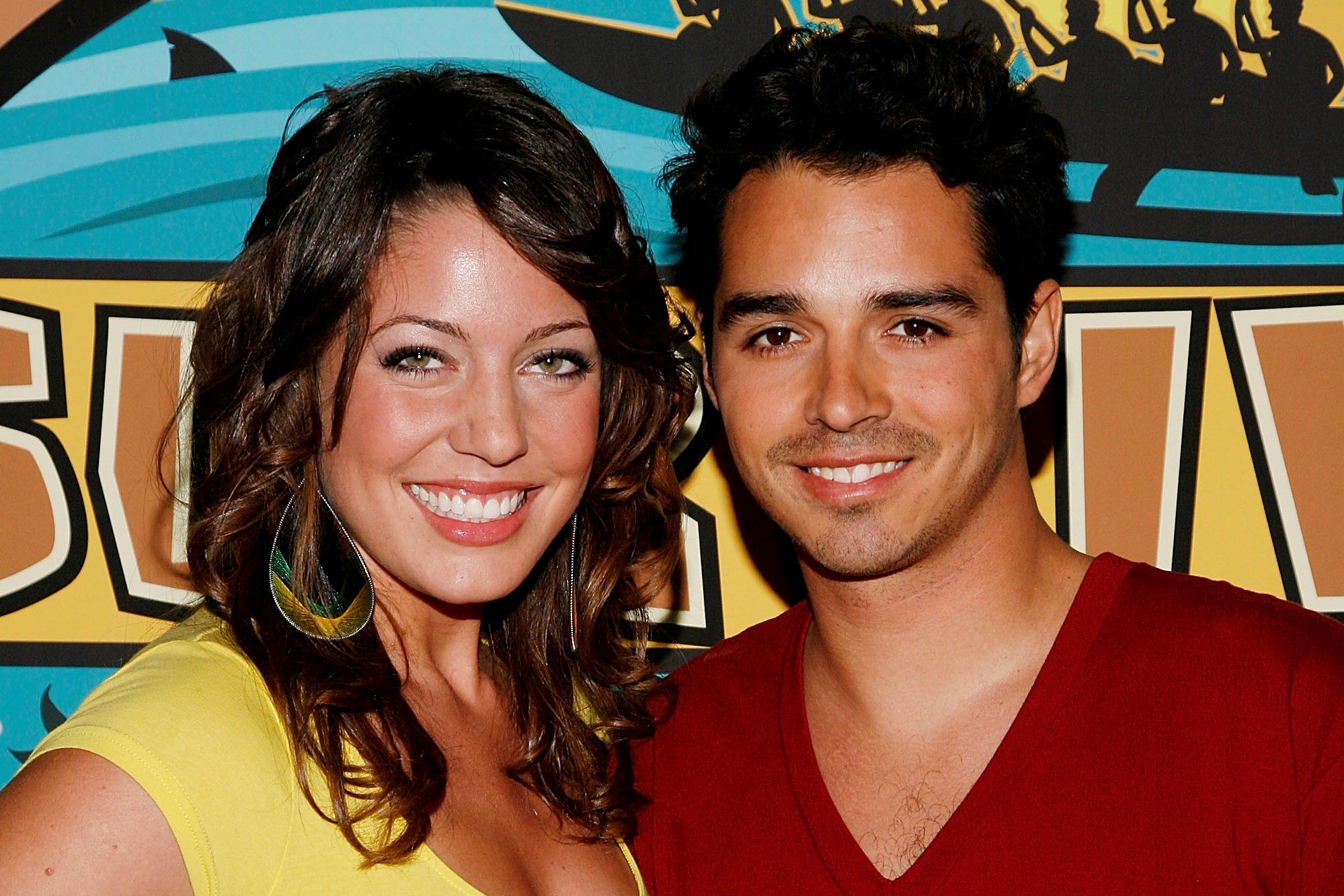 'Survivor' Season 16 castaways Amanda Kimmel and Ozzy Lusth pose for a picture together. Amanda wears a yellow shirt and big yellow and green earrings. Ozzy wears a red v-neck shirt.
