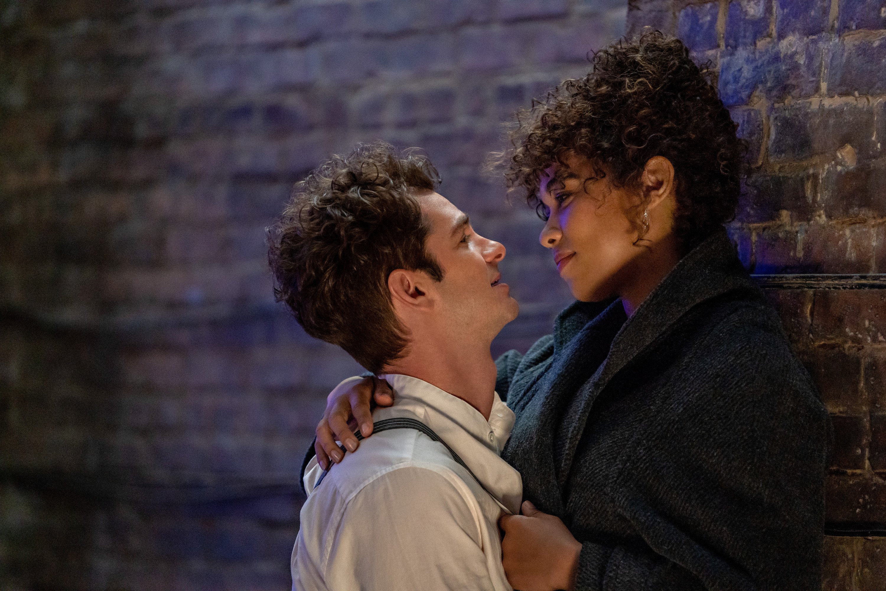 Andrew Garfield as Jonathan Larson, Alexandra Shipp as Susan in 'Tick, Tick...BOOM!' They embrace and look at each other lovingly while standing against a brick wall.