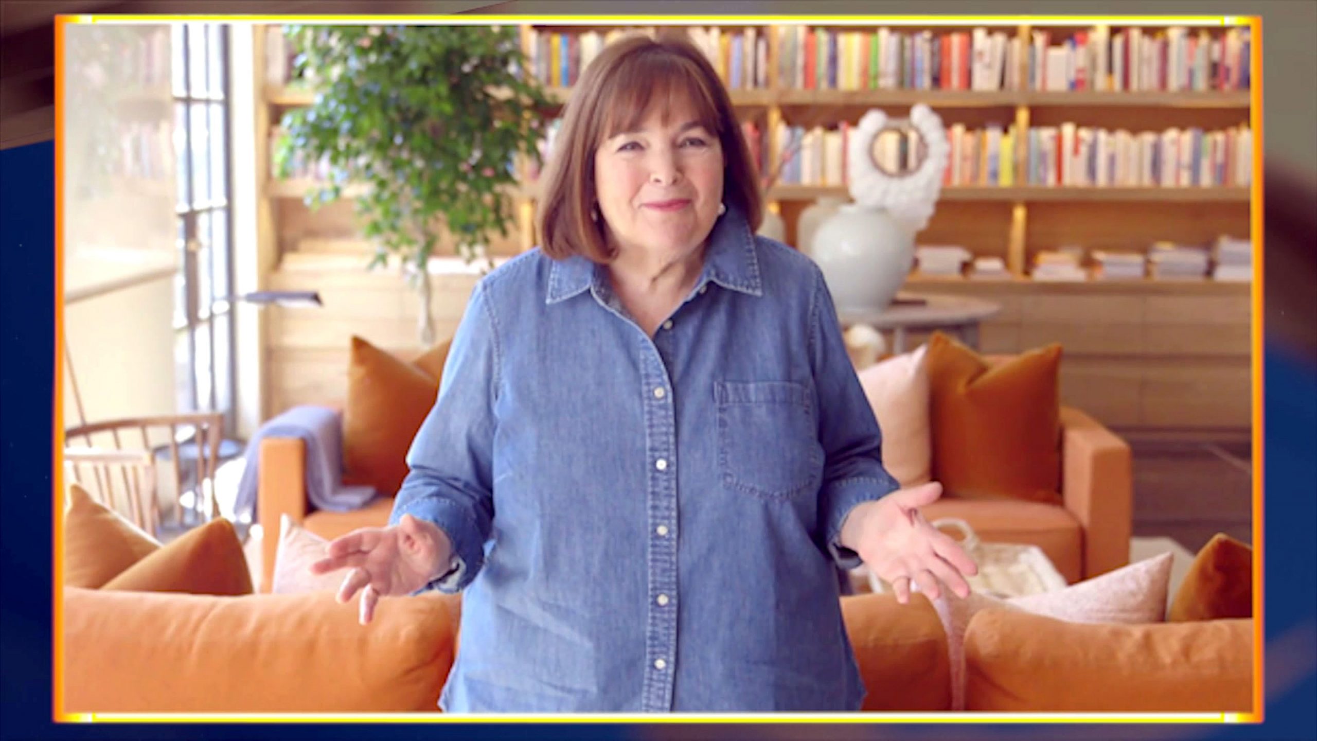 Ina Garten smirks with her hands out wearing a blue button down shirt