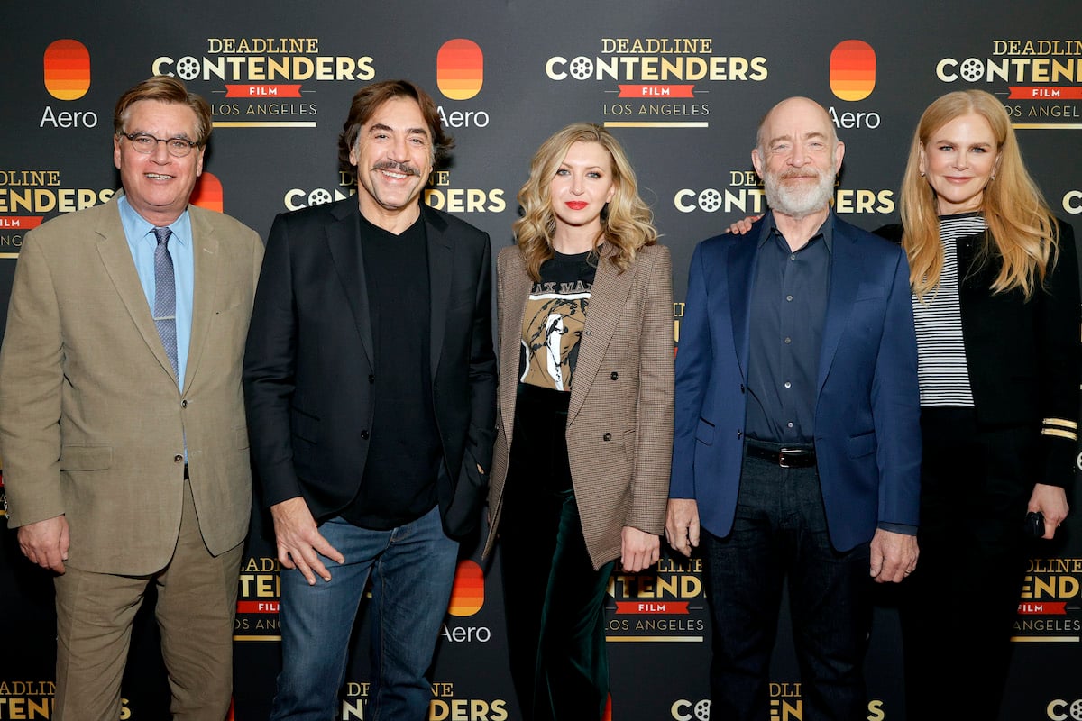 (L-R): Aaron Sorkin, Javier Bardem, Nina Arianda, J.K. Simmons, and Nicole Kidman from Amazon Studios' 'Being the Ricardos.' They stand side-by-side in front of a dark grey backdrop with red, white, and yellow text on it.