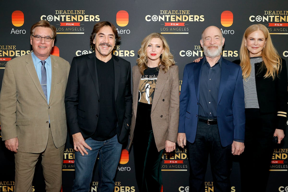 (L-R): Aaron Sorkin, Javier Bardem, Nina Arianda, J.K. Simmons, and  Nicole Kidman from Amazon Studios' 'Being the Ricardos.' They stand side-by-side in front of a dark grey backdrop with red, white, and yellow text on it.