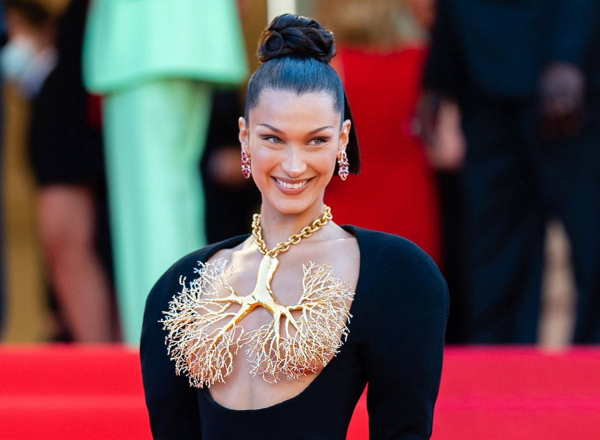 Bella Hadid wears a black dress and elaborate gold jewelry at an event.