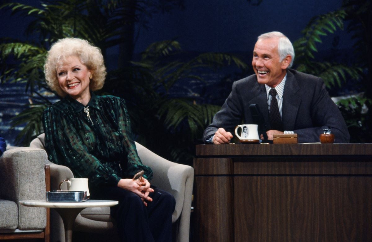 Betty White in a green shirt, Johnny Carson in a gray jacket, both laughing [c. 1986]