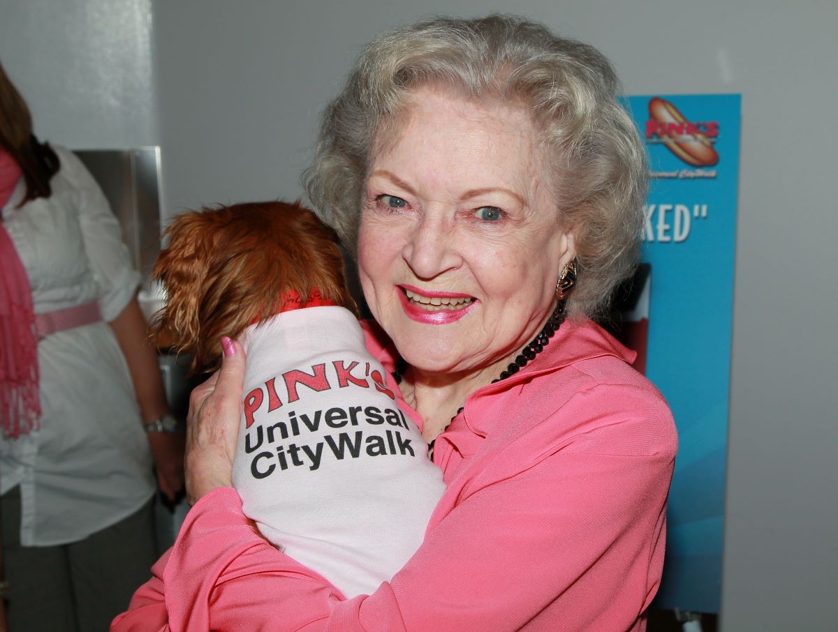 Betty White in a pink shirt, holding a dog and smiling