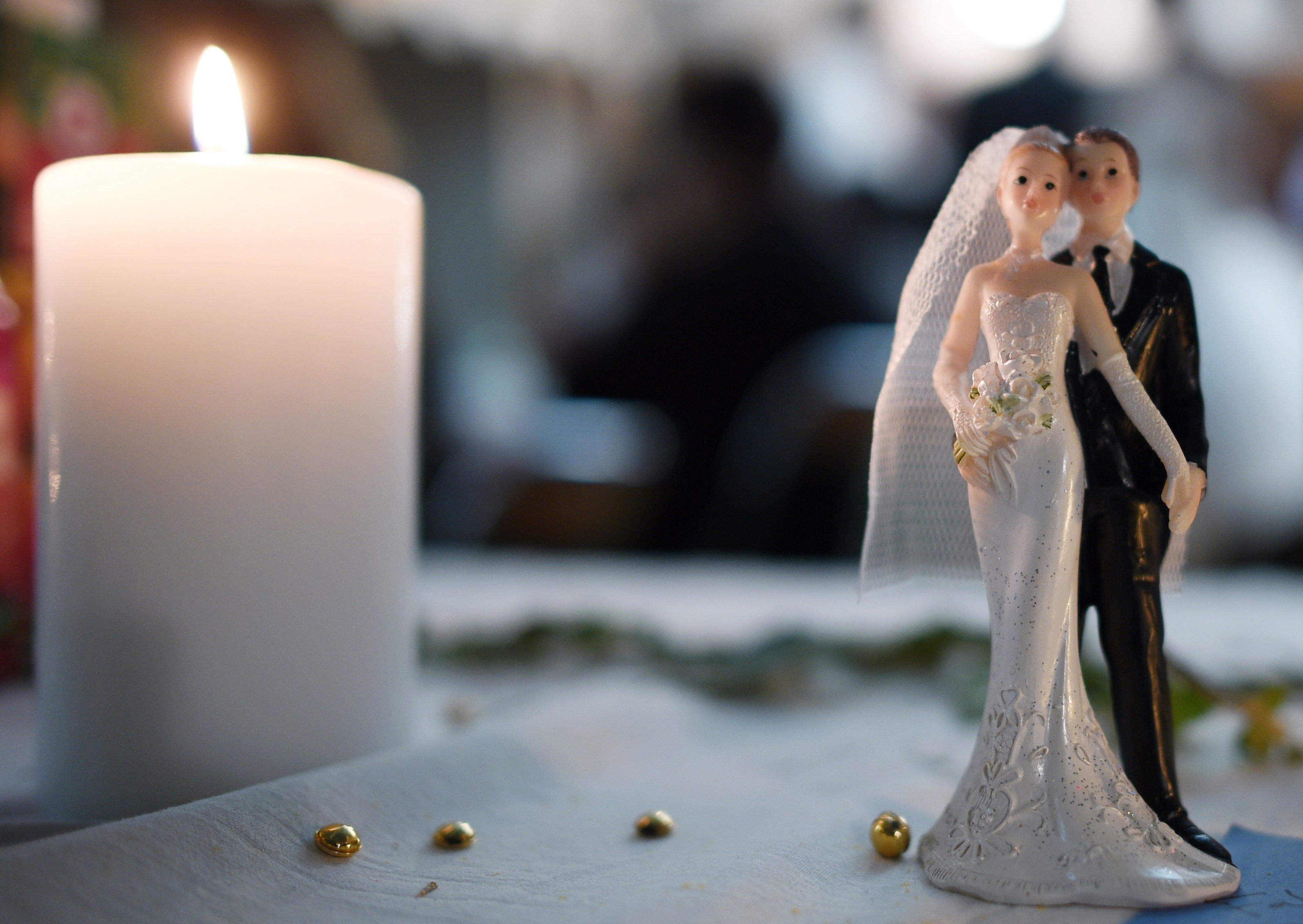 Bride and groom figurines next to a candle on a table