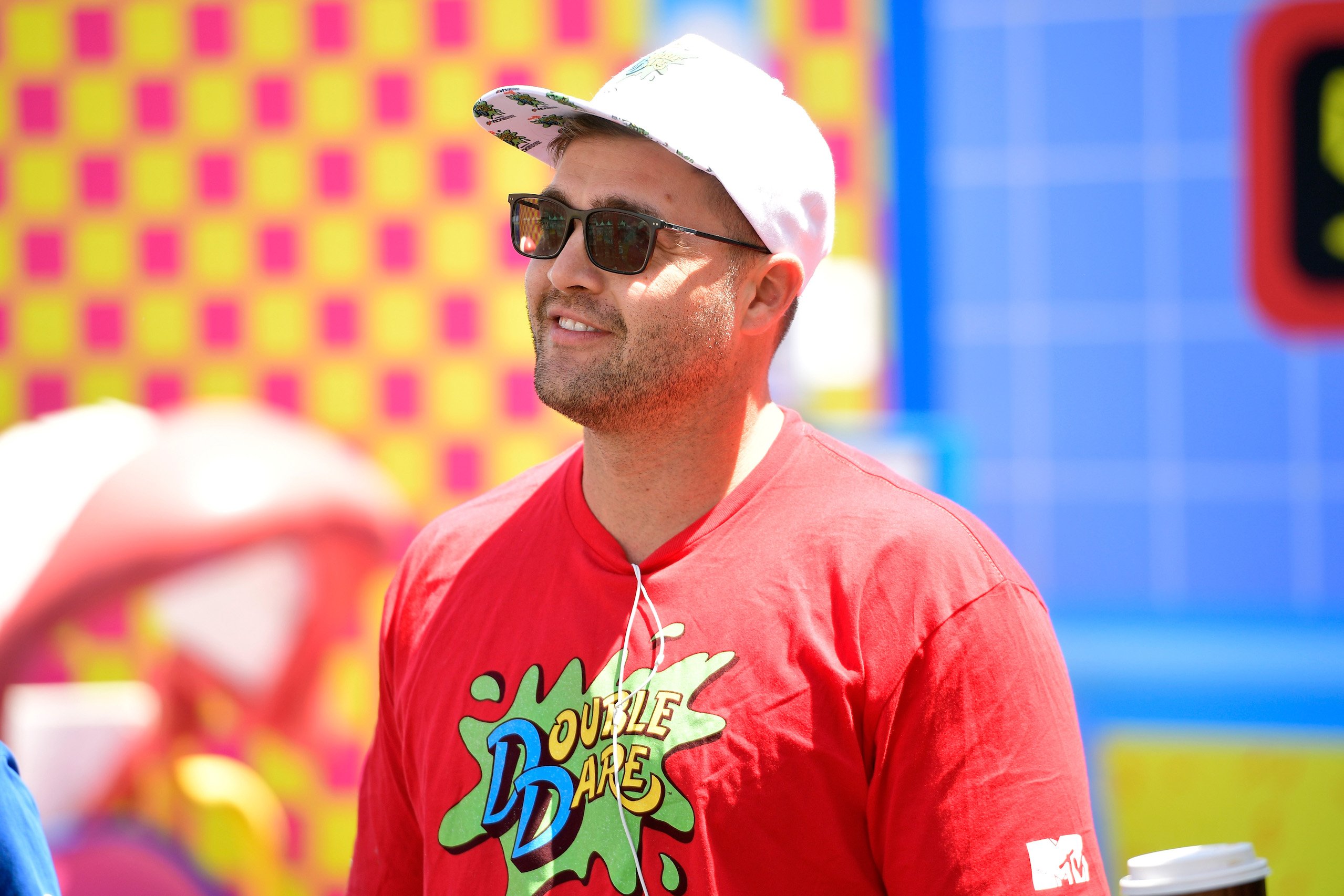 CT Tamburello from MTV's 'The Challenge' Season 37 smiling at a Double Dare event wearing a red shirt, white hat, and sunglasses