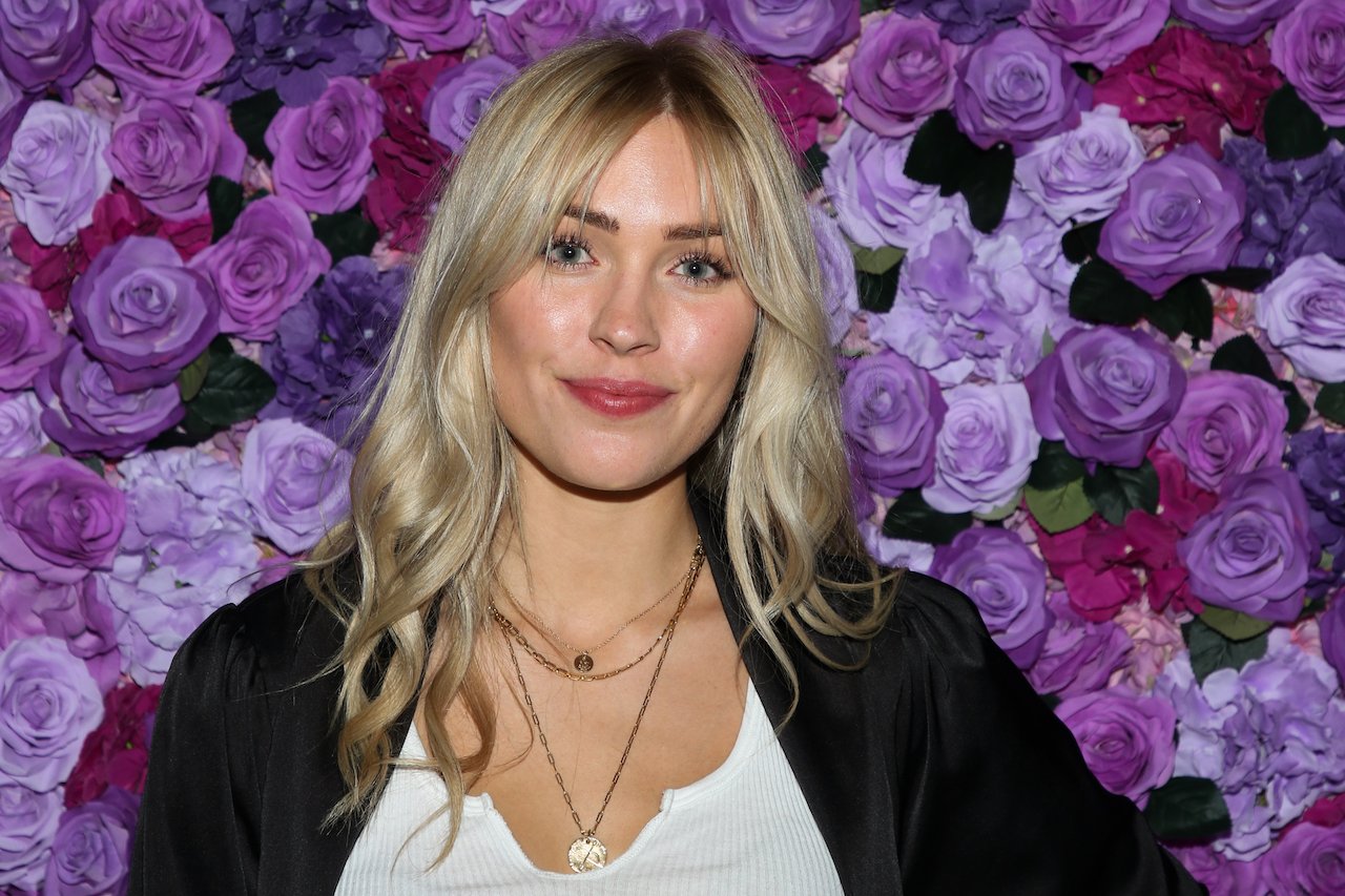Cassie Randolph smiles in front of a wall of purple flowers.