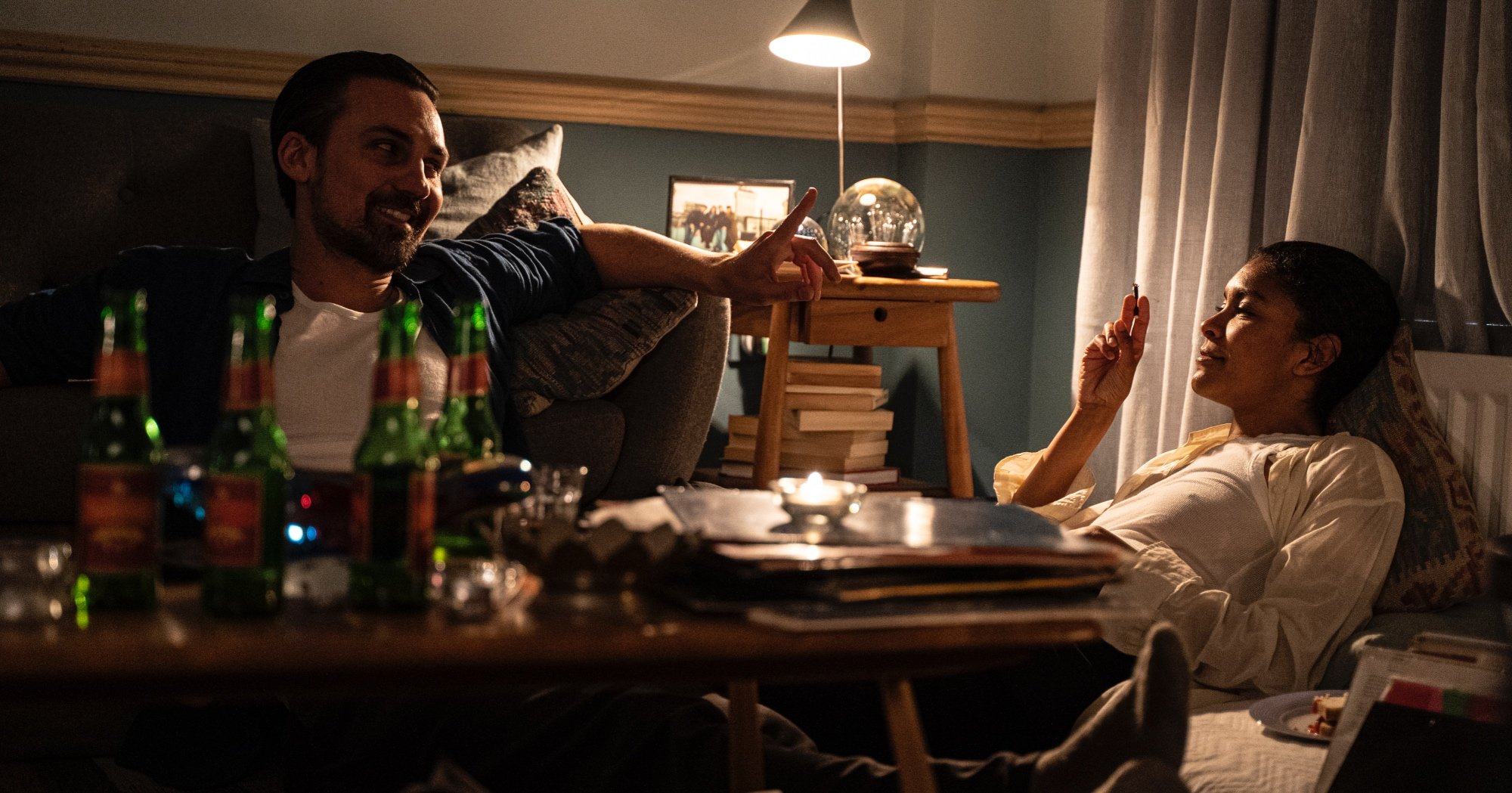 Characters Nathan Rose and Emily Baxter for AMC+'s 'Ragdoll' series sitting in living room smoking.