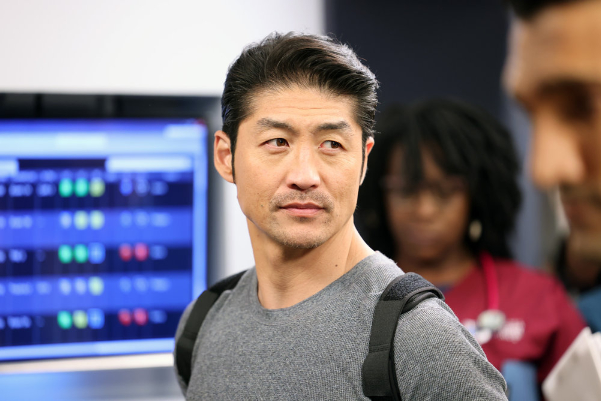 Brian Tee as Ethan Choi in Chicago Med Season 7. Choi is wearing a back brace and standing in front of a monitor.