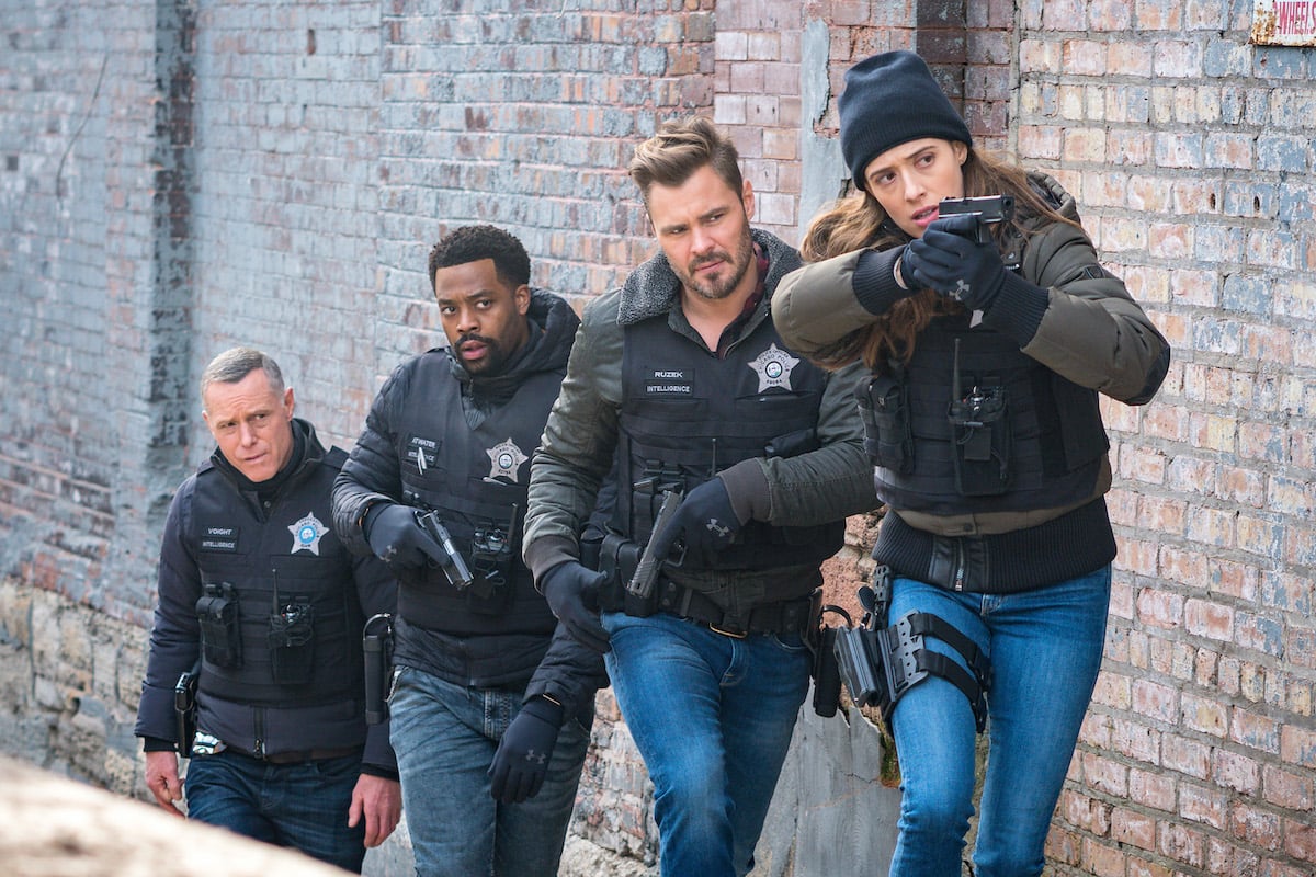 (L-R) Voight, Atwater, Ruzek, and Burgess walking alongside a brick wall, weapons drawn