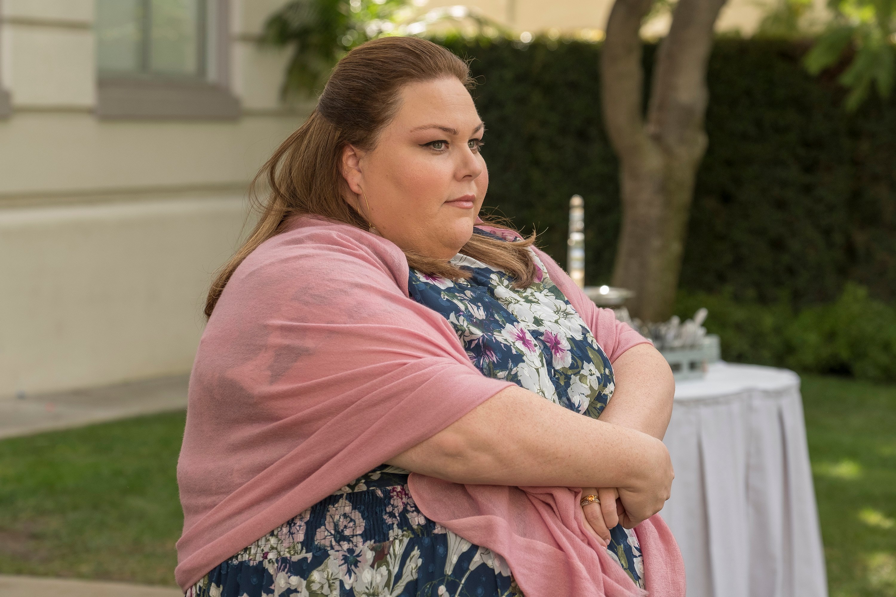 'This Is Us' Season 6 star Chrissy Metz, in character as Kate Pearson, wears a blue dress with white and pink flowers on it and a pink shawl.