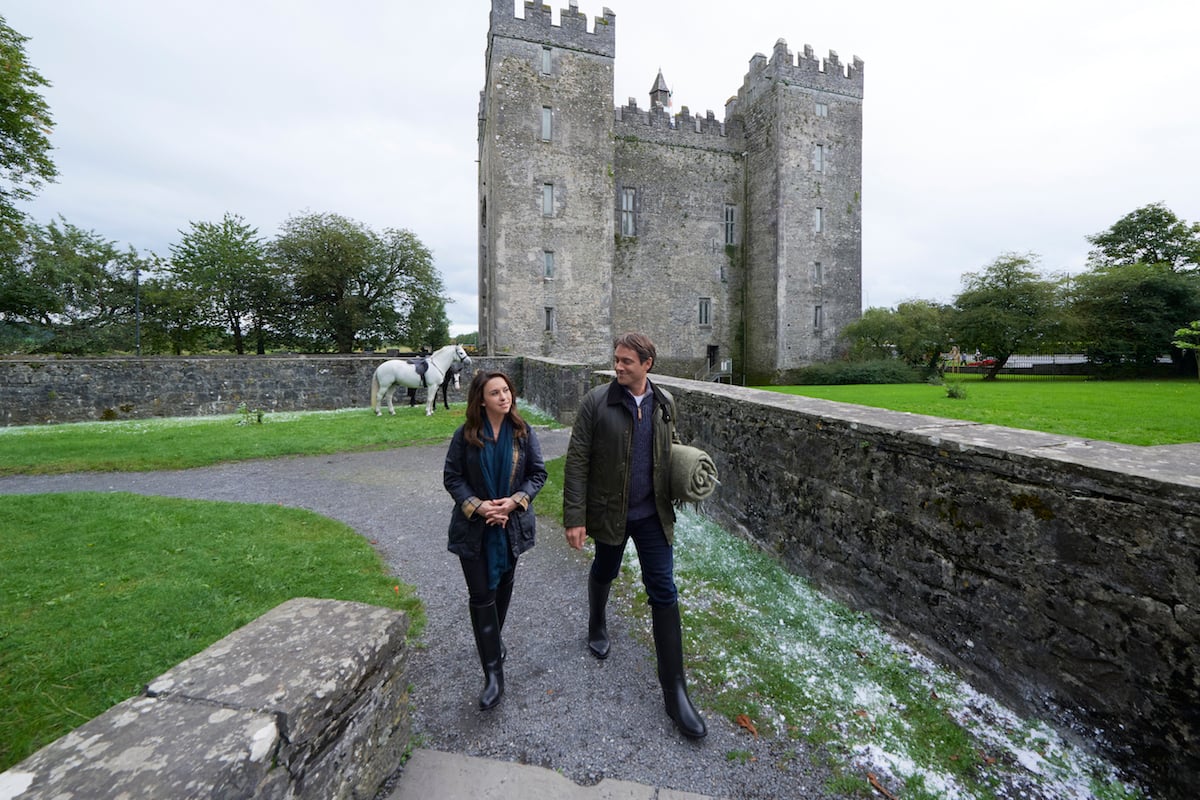 Lacey Chabert and Stuart Townsend walking outside of a castle in the Hallmark Channel movie 'Christmas at Castle Hart'