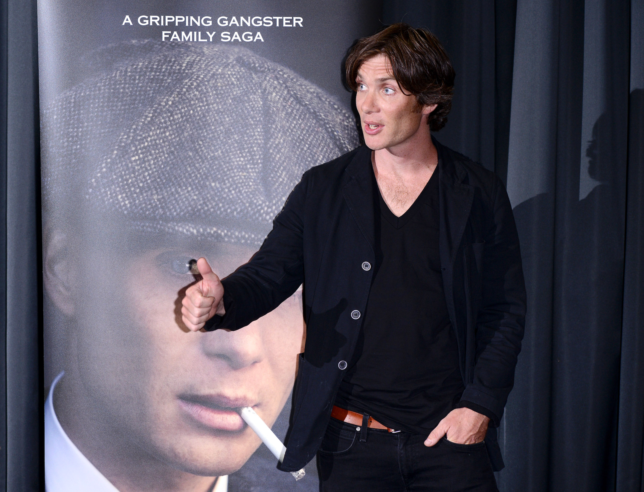 Cillian Murphy, the actor who plays Thomas Shelby in 'Peaky Blinders' Season 6, gesturing in front of a poster of Thomas Shelby
