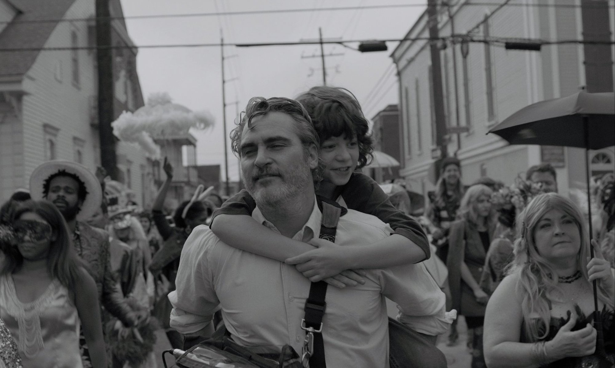 'C'mon C'mon' actors Joaquin Phoenix as Johnny and Woody Norman as Jesse walking through a crowd with Jesse on Johnny's back