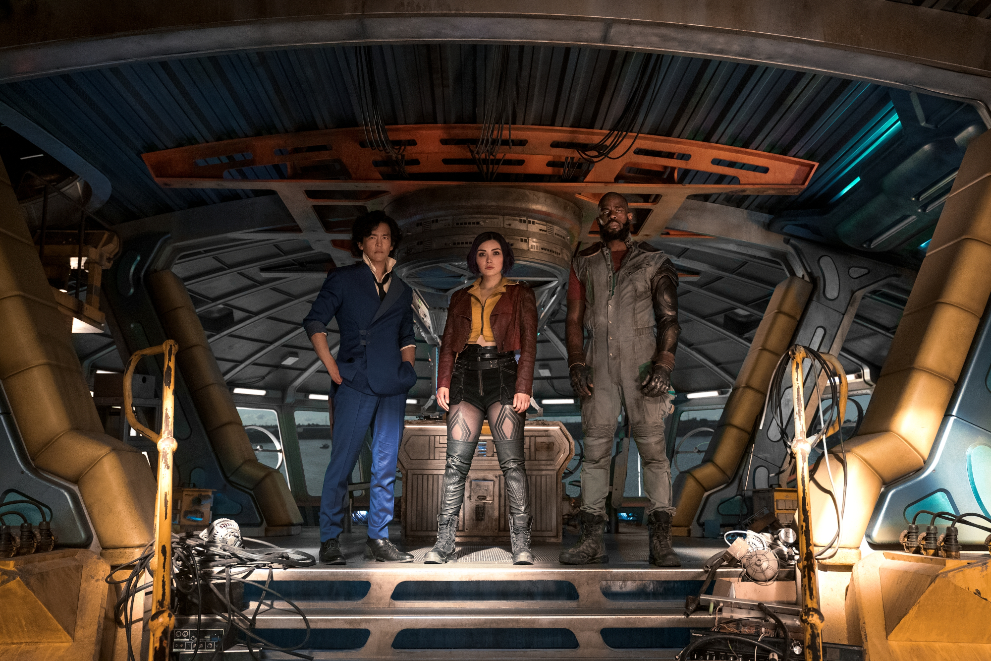John Cho, Daniella Pineda, and Mustafa Shakir in Netflix's live-action 'Cowboy Bebop.' They're standing side by side on the ship and facing the camera.