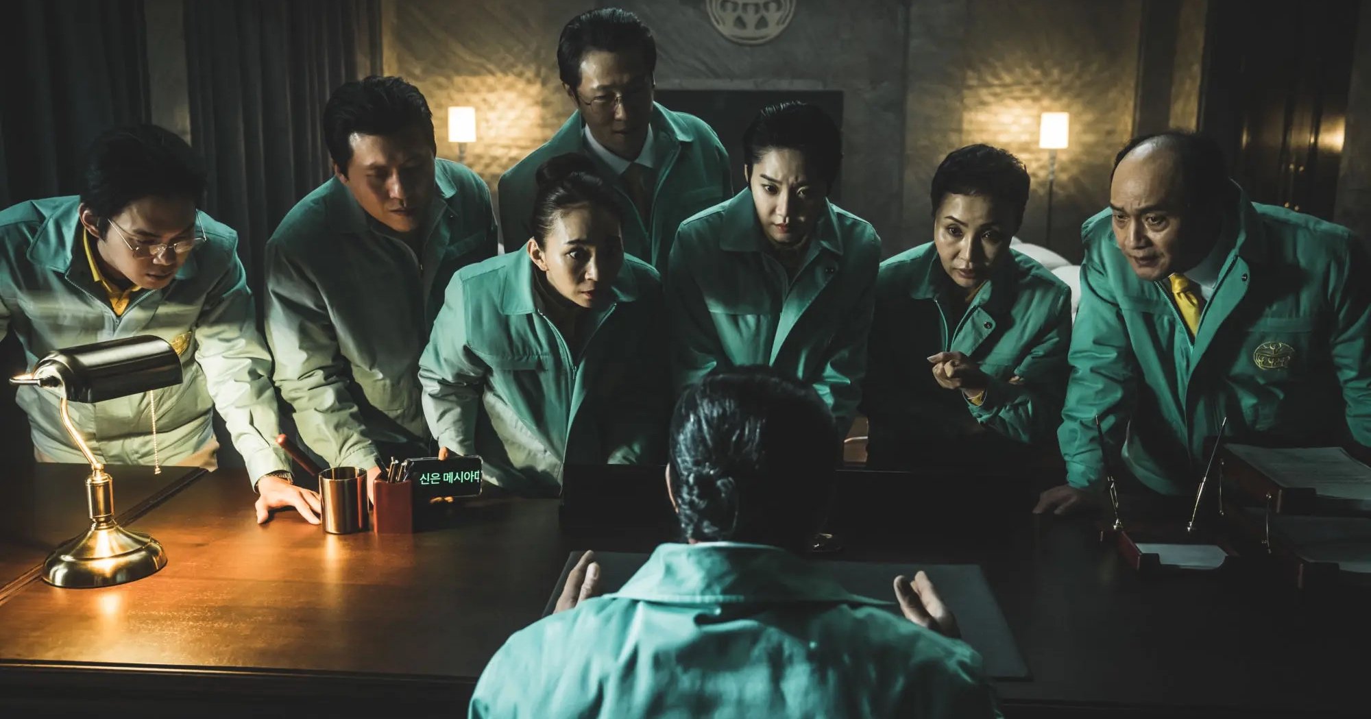 Cult followers in 'Hellbound' for Netflix wearing mint green jackets huddling over desk.
