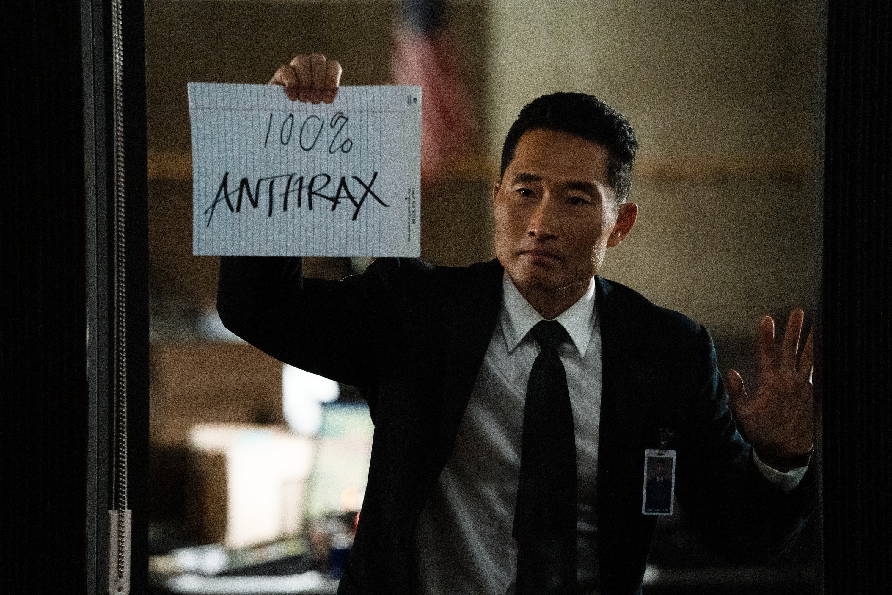Daniel Dae Kim holding up a hand-written sign reading '100% anthrax' in 'The Hot Zone: Anthrax'