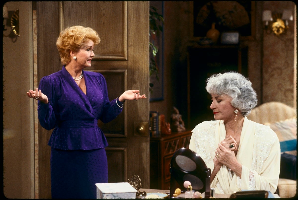 'The Golden Girls' actor Debbie Reynolds in a blue dress and Bea Arthur in a white dress; standing in a bedroom.
