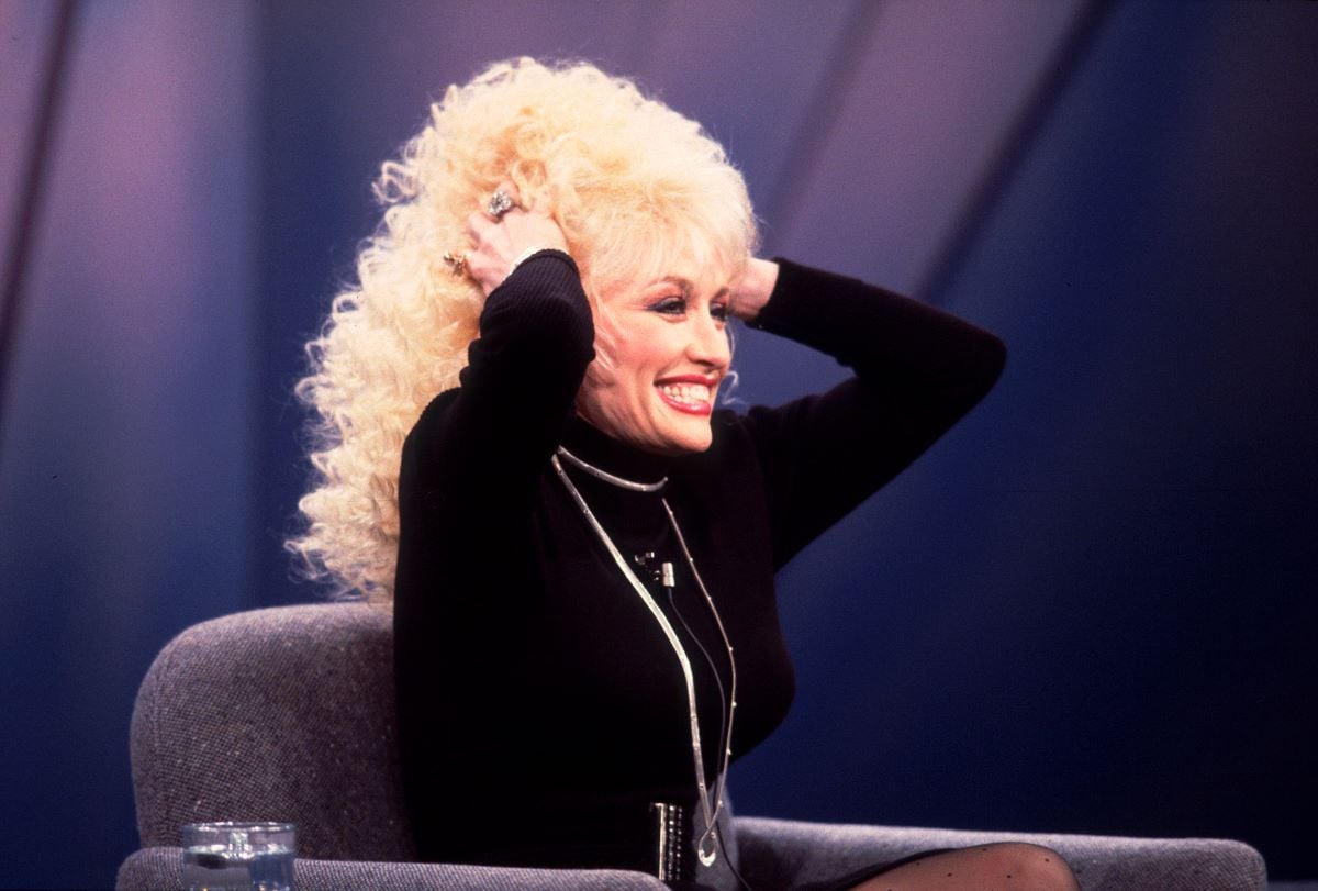 Dolly Parton, seated in black with her hands in her hair