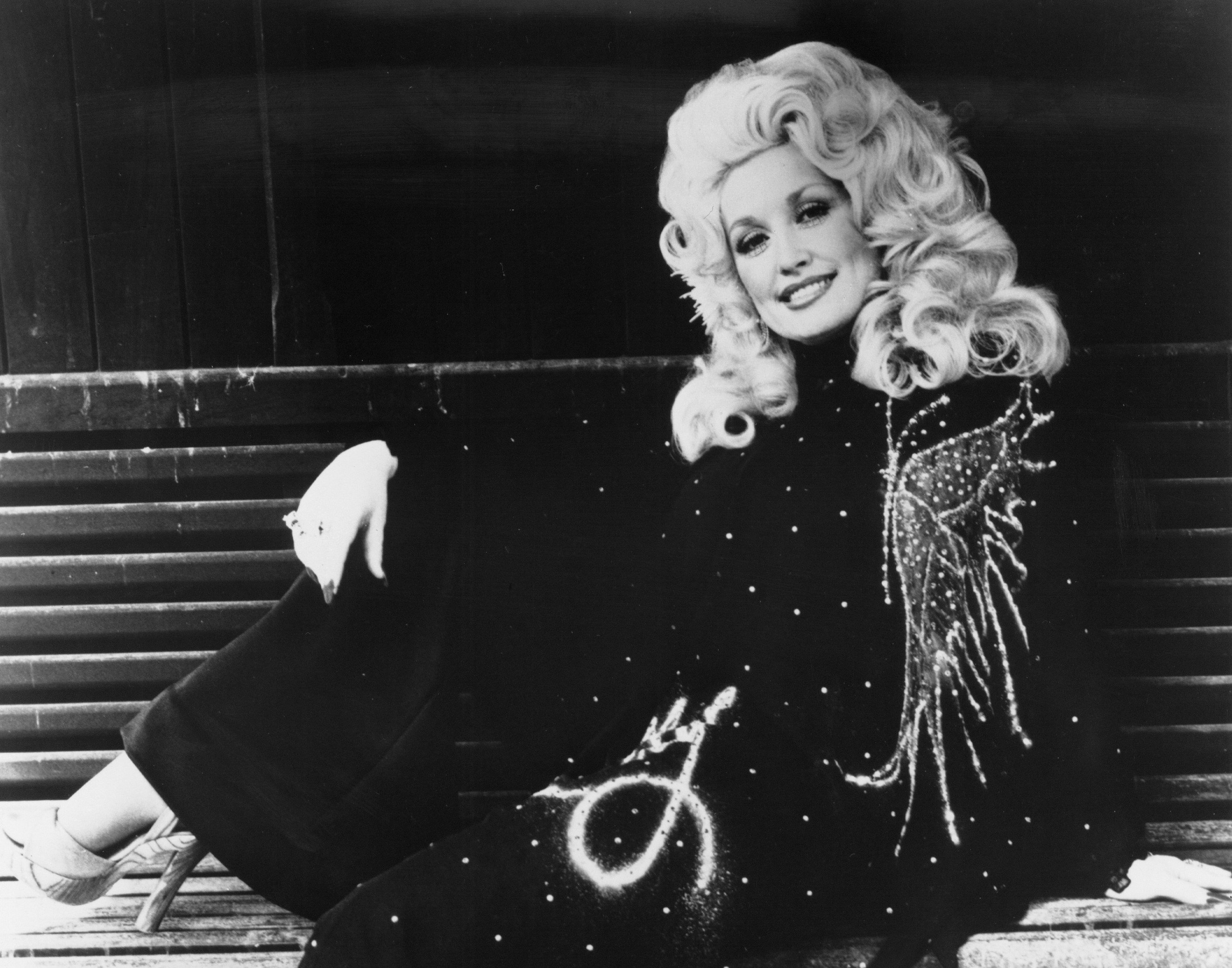 A black and white photo of Dolly Parton wearing a black jumpsuit with a white butterfly. 