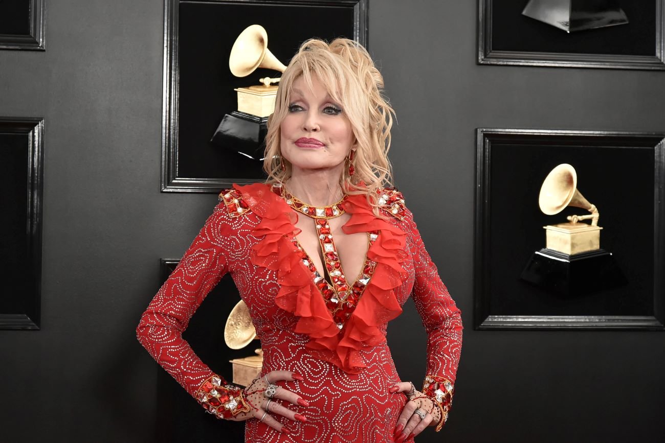 Dolly Parton wears a red bedazzled dress with a ruffled collar. 