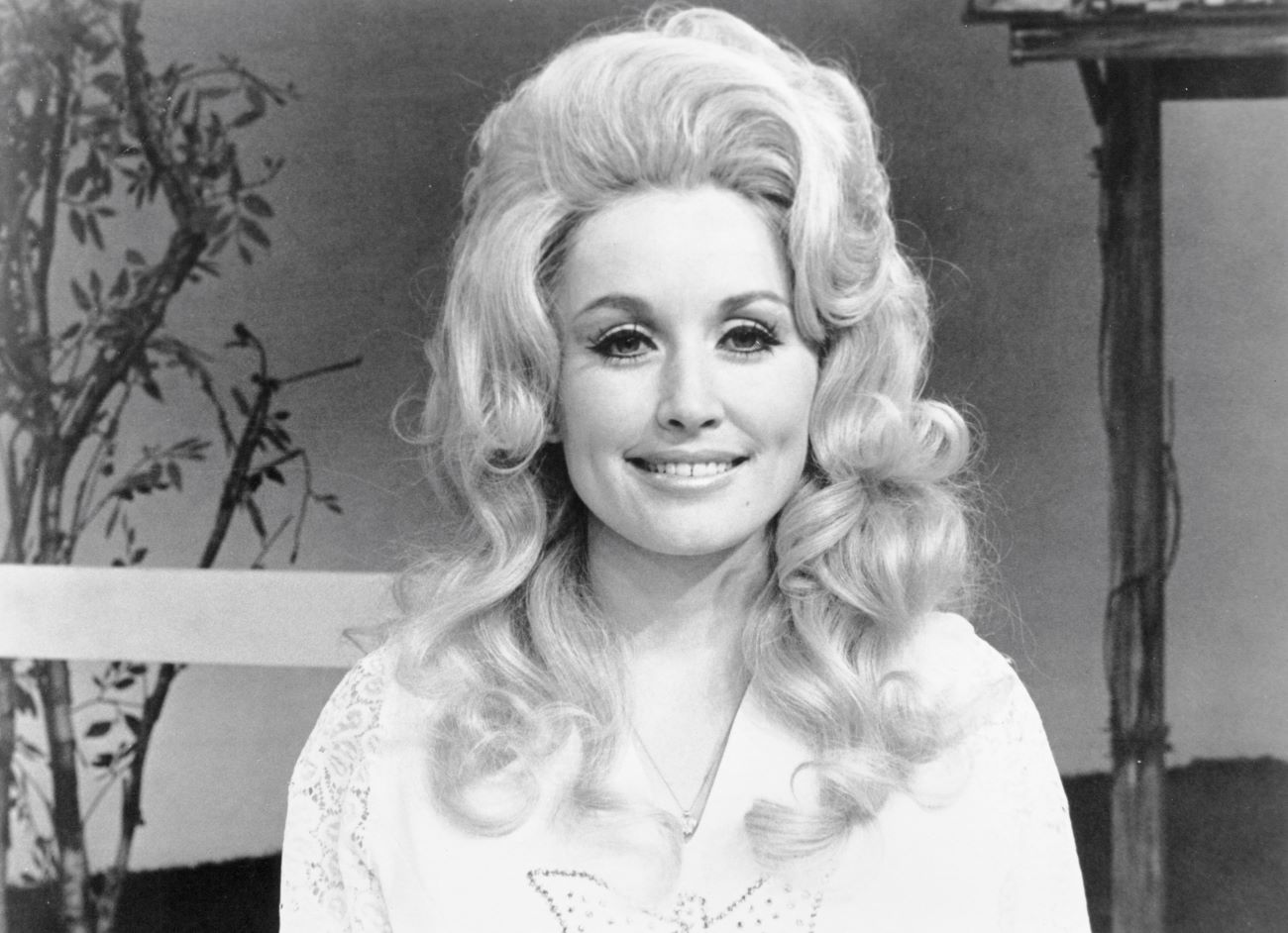 A black and white photo of Dolly Parton wearing a rhinestoned white shirt.